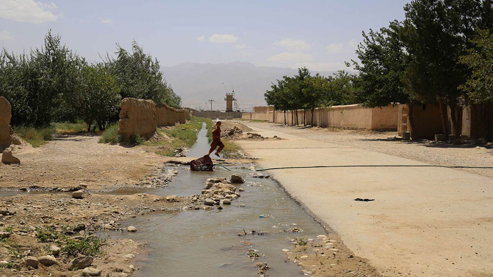 A boy jumps over a stream that flows out of the walls of the Bagram base