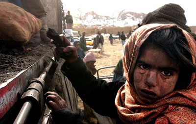 Covered in coal dust, an Afghan girl grabs spilled charcoal at an aid relief distribution in Kabul