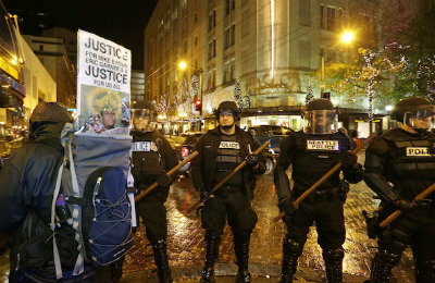 Police with wooden sticks stand guard next to a protester for Eric Garner and Mike Brown in downtown Seattle