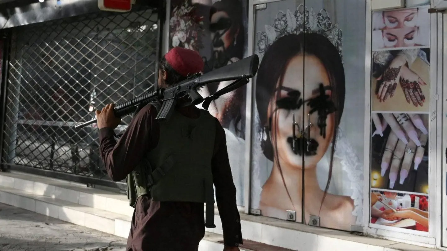 Taliban fighter walks past a beauty salon with images of women defaced using spray paint 